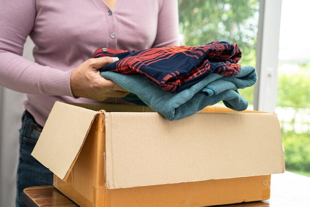 Kledingdonatiedoos met gebruikte kleding en pop thuis vasthouden om hulp te bieden aan arme mensen in de wereld