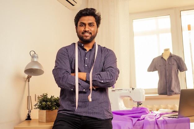 Kleermaker aziatische man ontwerper naaien kleding op naaimachine naast laptop studio werkplek
