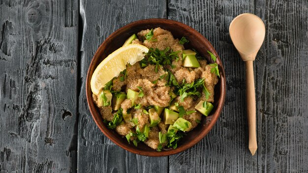 Klei kom met amarant zaad salade met avocado, citroen en peterselie op een donkere houten tafel