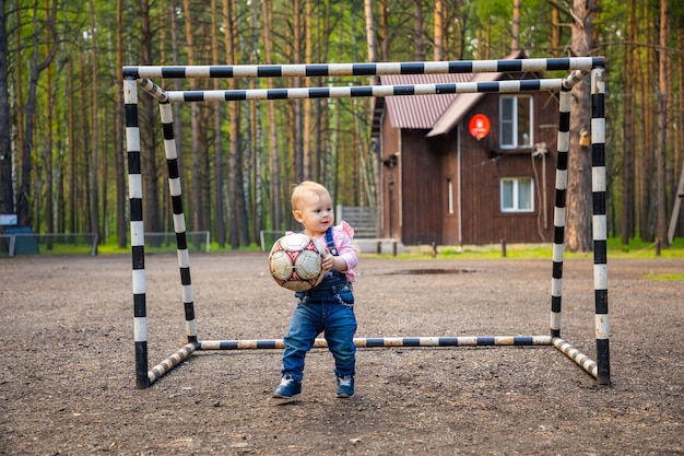 Klein actief meisje baby blond spelen met voetbal bal in het bos Rusland