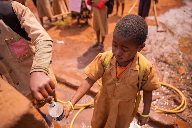 Klein Afrikaans schoolmeisje verzamelt water in de fles uit de kraan van de fontein op het schoolplein