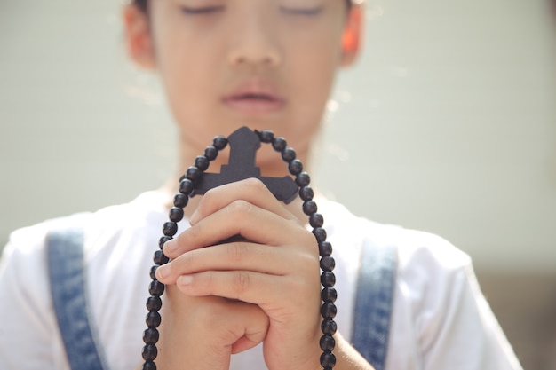 Foto klein aziatisch meisje bidden met het kruis vast te houden, christelijk concept.