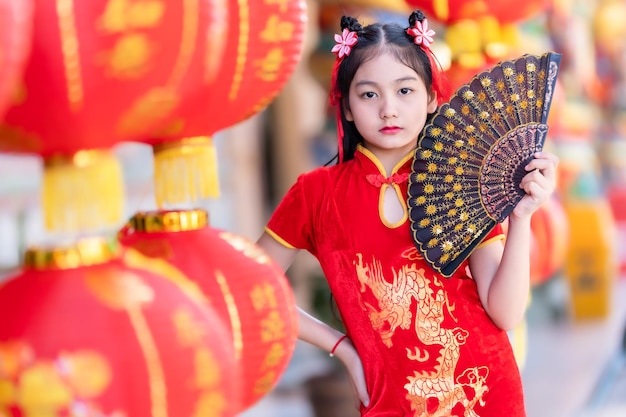 Klein Aziatisch meisje dat rode traditionele Chinese cheongsam draagt en een Fanningand-lantaarn vasthoudt met het Chinese alfabet Zegeningen erop geschreven Is een gelukszegen compliment decoratie voor Nieuwjaar