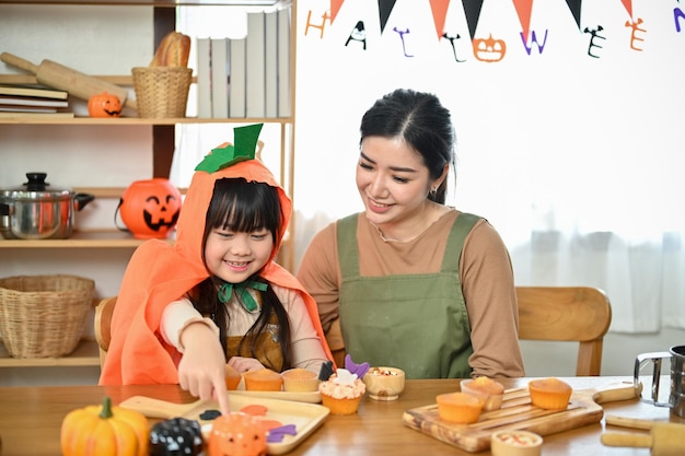 Klein Aziatisch meisje geniet van het maken en decoreren van Halloween cupcakes met haar moeder