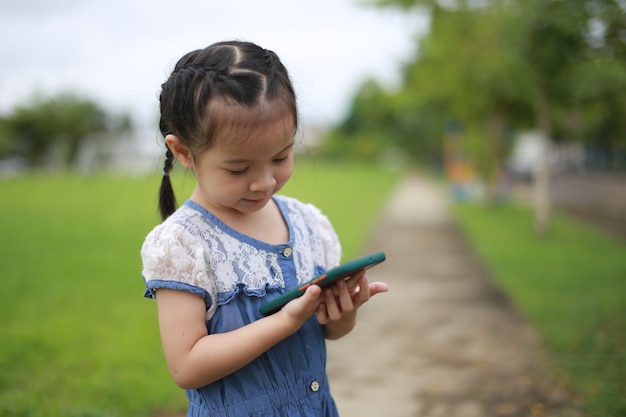 Klein Aziatisch meisje met een smartphone buiten.
