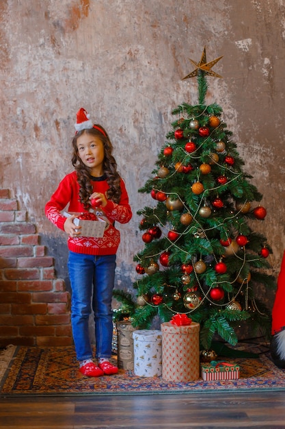 Klein Aziatisch meisje versiert kerstboom glimlachend Kerstmis, nieuwjaar