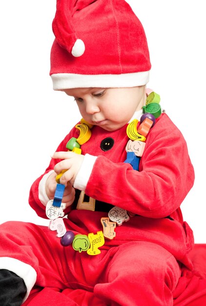 Foto klein babymeisje dat het kostuum van de kerstman draagt en met houten kralen speelt op witte achtergrond