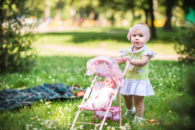 Klein babymeisje die op gras lopen en stuk speelgoed wandelwagen met pop rollen