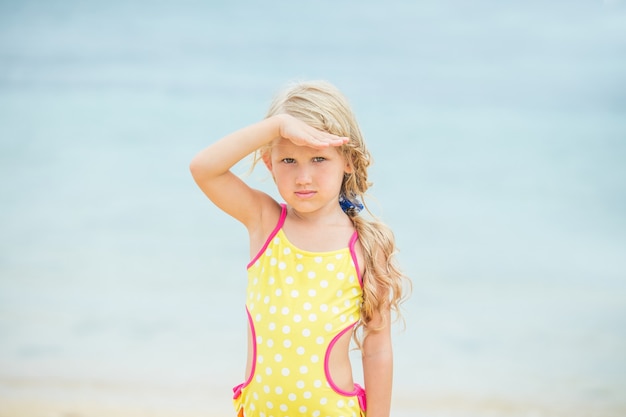 Klein babymeisje is mooi en gelukkig in een helder zwempak in de middag op een zonnig strand