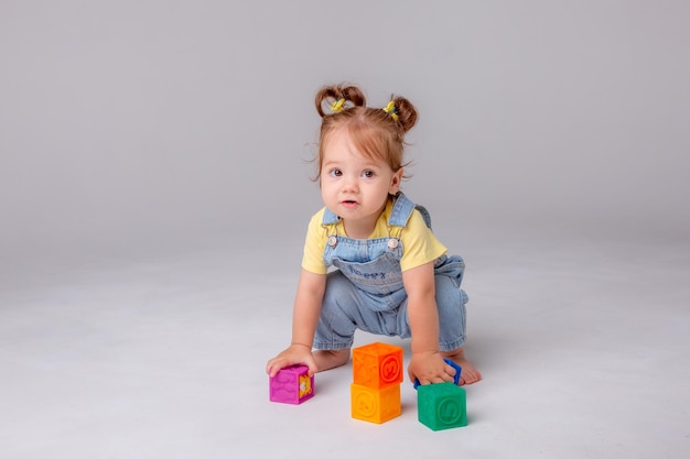 klein babymeisje is op een witte achtergrond en speelt met kleurrijke blokjes Kid's Play Toy Cubes