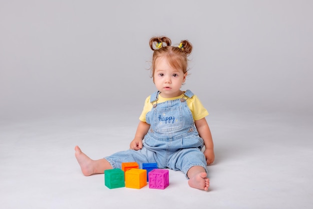 klein babymeisje zit op een witte achtergrond en speelt met kleurrijke kubussen. kinderspeelgoed