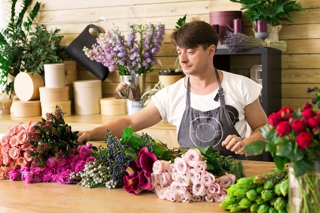 Klein bedrijf. mannelijke bloemist rozen boeket maken in bloemenwinkel. man assistent of eigenaar in bloemenwinkel, decoraties en arrangementen maken. bloemen bezorgen, orde scheppen