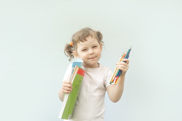 Klein blank kindmeisje van vijf jaar oud, krullend blond meisje met kleurpotloden in haar handen. Het concept van de creativiteit en voorbereiding van kinderen op school.