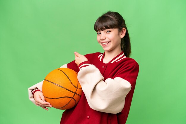 Klein blank meisje dat basketbal speelt over een geïsoleerde achtergrond die naar achteren wijst