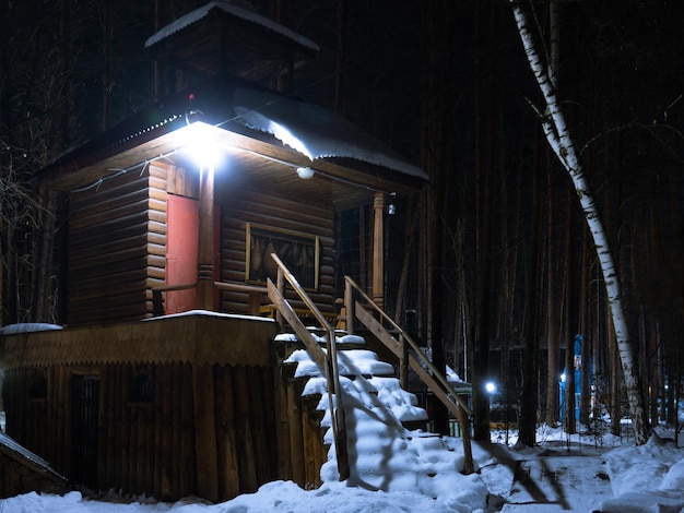 Klein blokhuis in een winter besneeuwd bos 's nachts De trap die naar het huis leidt is bedekt met sneeuw De lantaarn hangt boven de deur van het huis Klein fort in het winterbos