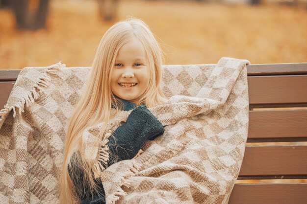 klein blond meisje in een plaid in het park op een bankje