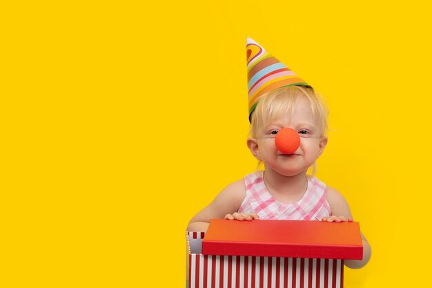 Klein blond meisje in vakantiehoed met cadeau en lachend Verjaardag 1 jaar