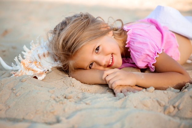 klein blond meisje liggend op een zandstrand lachend