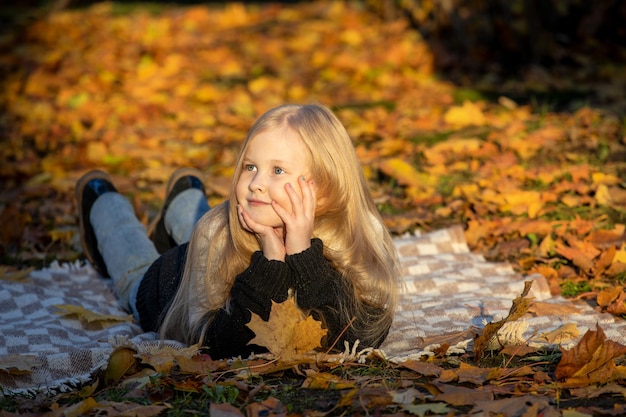 Klein blond meisje ligt in de herfst op een deken in het park