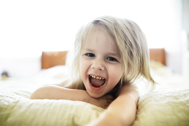 Klein blond meisje ligt op het bed Emotioneel kind baby poseren