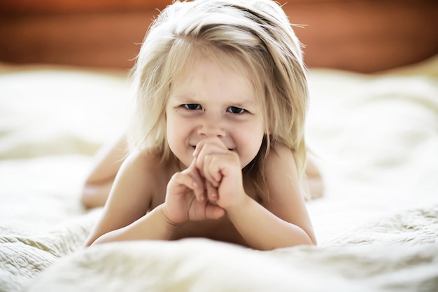 Klein blond meisje ligt op het bed Emotioneel kind baby poseren