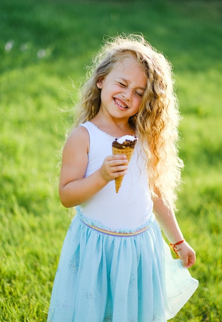Klein blond meisje met lang haar heeft plezier met het eten van ijs in een zomerpark.