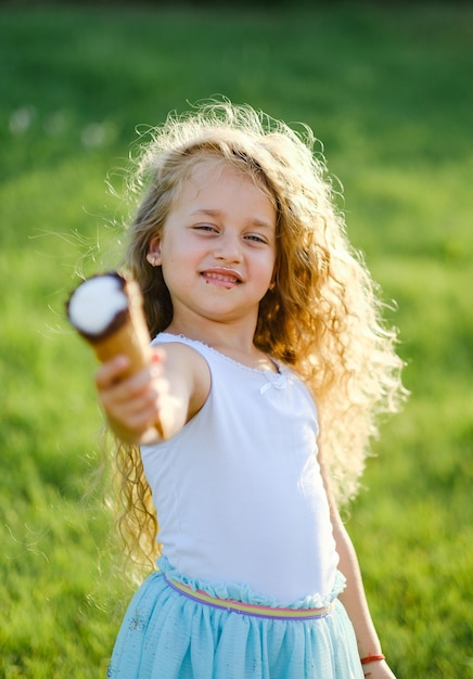 Klein blond meisje met lang haar heeft plezier met het eten van ijs in een zomerpark.