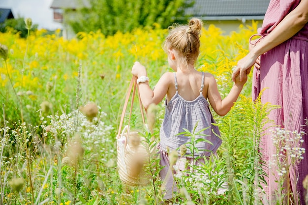 klein blond meisje met tas met mama's hand in geel veld