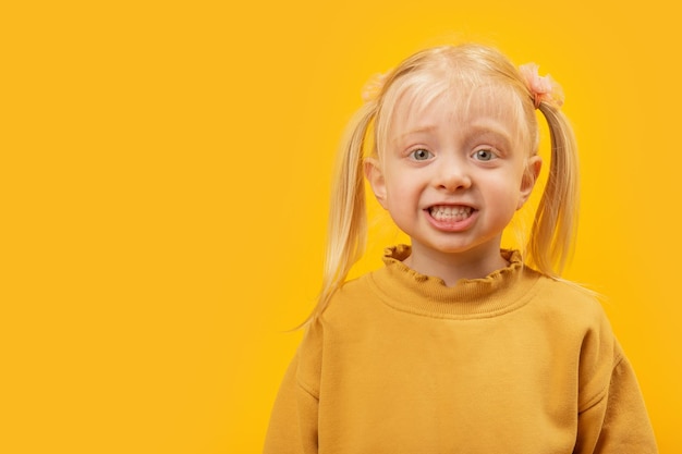 Klein blond meisje met twee paardenstaarten in geel shirt glimlacht en kijkt naar de camera Studiofoto met lege ruimte voor reclamemodel