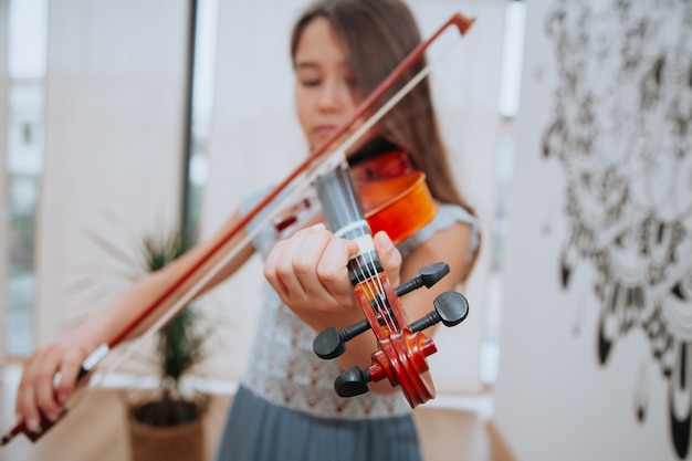 Klein brunette meisje in een mooie jurk die binnen viool speelt Muziekinstrumenten concept