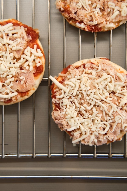 Klein diepgevroren pizza-halffabrikaat met tomatensaus en kaas op de grill, bereid om te bakken