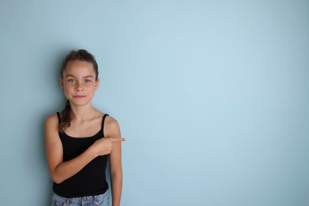 Klein emotioneel tienermeisje in een zwart t-shirt 11 12 jaar oud op een geïsoleerde blauwe achtergrond Children39s studioportret Plaats de tekst om de plaats voor de inscriptie te kopiëren