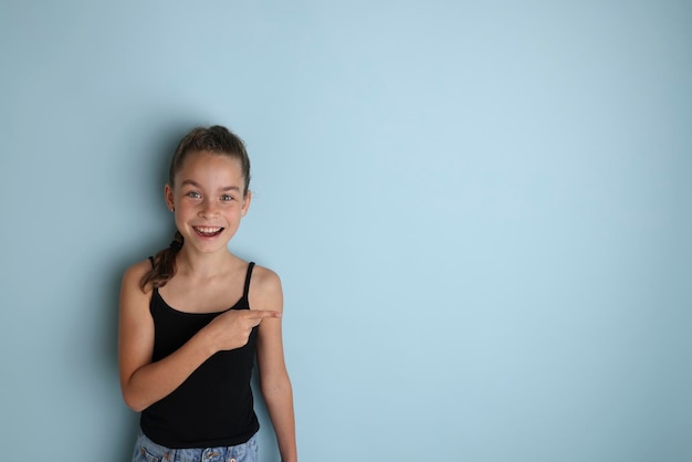 Klein emotioneel tienermeisje in een zwart t-shirt 11 12 jaar oud op een geïsoleerde blauwe achtergrond Children39s studioportret Plaats de tekst om de plaats voor de inscriptie te kopiëren