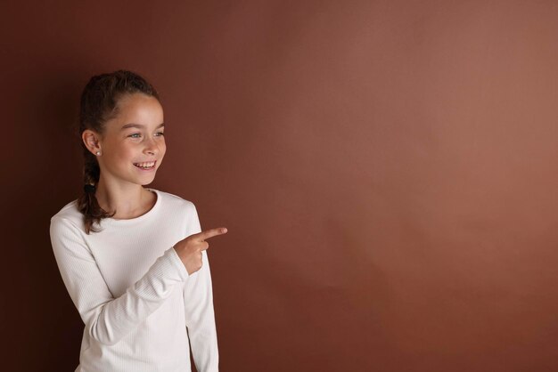 Klein emotioneel tienermeisje in het wit 11 12 jaar oud op een geïsoleerde bruine chocolade achtergrond