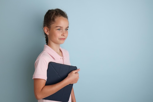 Klein emotioneel tienermeisje in roze shirt 11 12 jaar oud op een geïsoleerde blauwe achtergrond met een tablet in haar handenChildren39s studio portret Plaats de tekst om de plaats voor de inscriptie te kopiëren