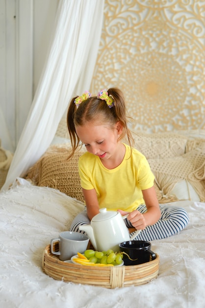 klein gelukkig meisje dat ontbijt eet en thee drinkt met fruit vrolijk kind