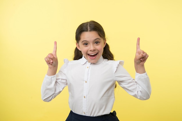 Klein genie heeft een idee. gelukkig meisje houdt vingers aan de orde gesteld op gele achtergrond. terug naar school. kleine kindglimlach met inspiratie. goed idee. gewoon geïnspireerd. zorgeloze schoonheid.