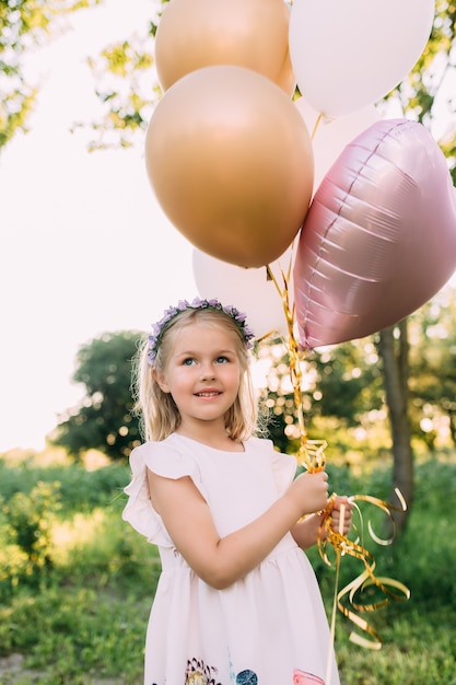 Klein glanzend meisje met roze ballonnen in de tuin.