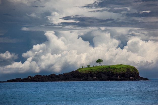 Klein groen eiland in Indische Oceaan. Contrast bewolkte hemel en kalme zee-oppervlak. Krachtig en rustig natuurlandschap.