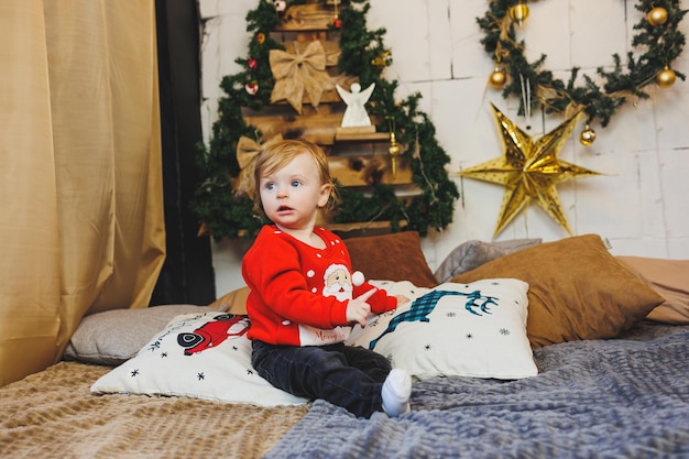 klein jongetje bij de kerstboom een idee voor een kinderfoto voor de nieuwjaarsstudio Nieuwjaarsdecoratie Kerstcadeaus rood feestelijk kinderkostuum