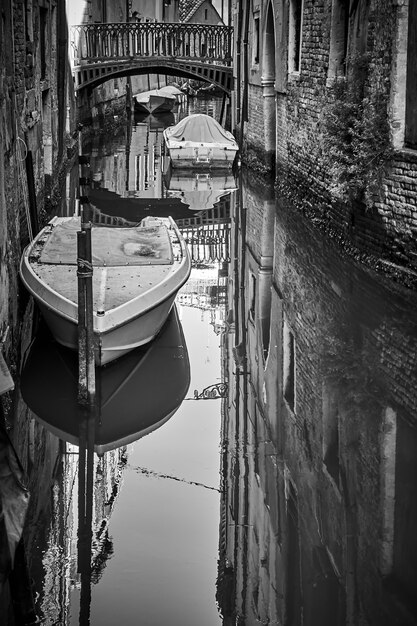 Klein kanaal in Venetië met brug en afgemeerde boten, Italië. Zwart-wit stadsfotografie, Venetiaans uitzicht