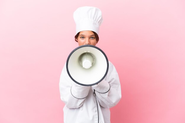 Klein kaukasisch chef-kokmeisje dat op roze achtergrond schreeuwt door een megafoon