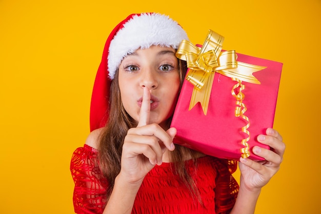 Klein kaukasisch meisje met een kerstcadeautje en vraagt de camera om stilte met haar vinger in haar mond