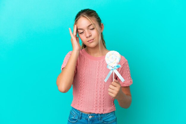 Klein Kaukasisch meisje met een lolly geïsoleerd op een blauwe achtergrond met hoofdpijn