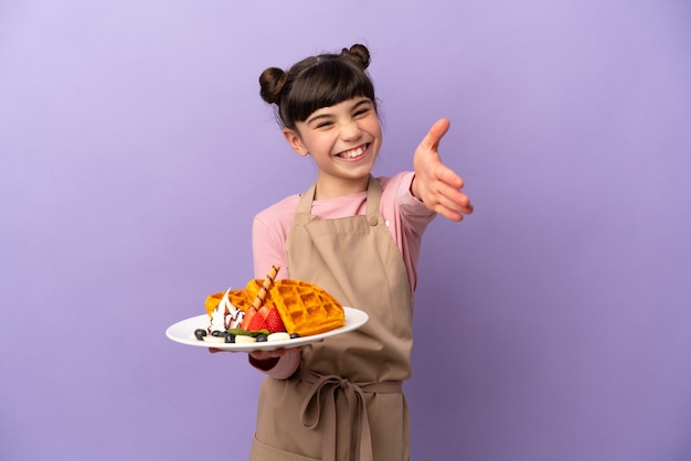 Klein Kaukasisch meisje met wafels geïsoleerd op paars handen schudden voor het sluiten van een goede deal