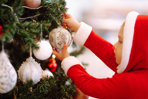 Klein kind dat decoratieve speelgoedbal aan de kerstboomtak hangt.