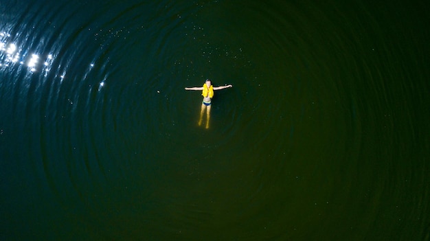 Klein kind dat in het reddingsvest zwemt Een jongen die een geel levensreddend opblaasbaar vest op waterachtergrond draagt Luchtconcept
