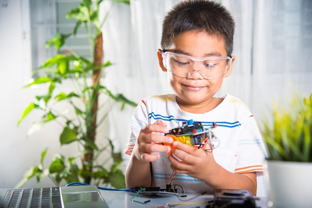 Klein kind dat probeert een wiel te bouwen tot een speelgoedwagen Aziatische jongen die een wiel assembleert tot een Arduino robot auto huiswerk het creëren van elektronische AI-technologie workshop online schoolles