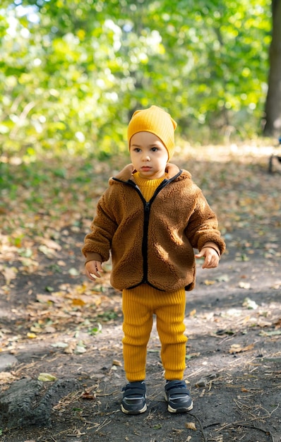 Klein kind draagt een bruin jasje en een gele broek Een klein kind gekleed in een bruin jasje en een gele broek staat alleen