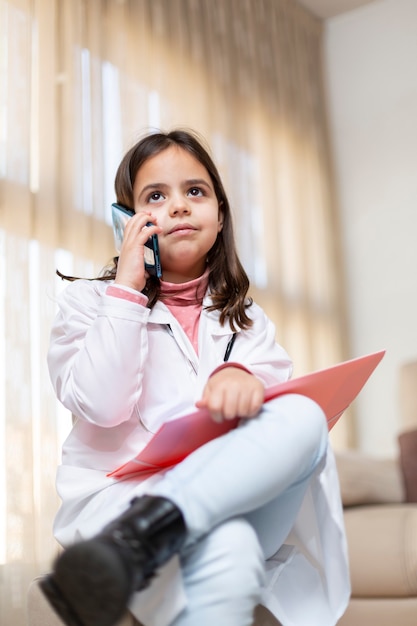 Klein kind gekleed in uniform verpleegster praten op mobiele telefoon